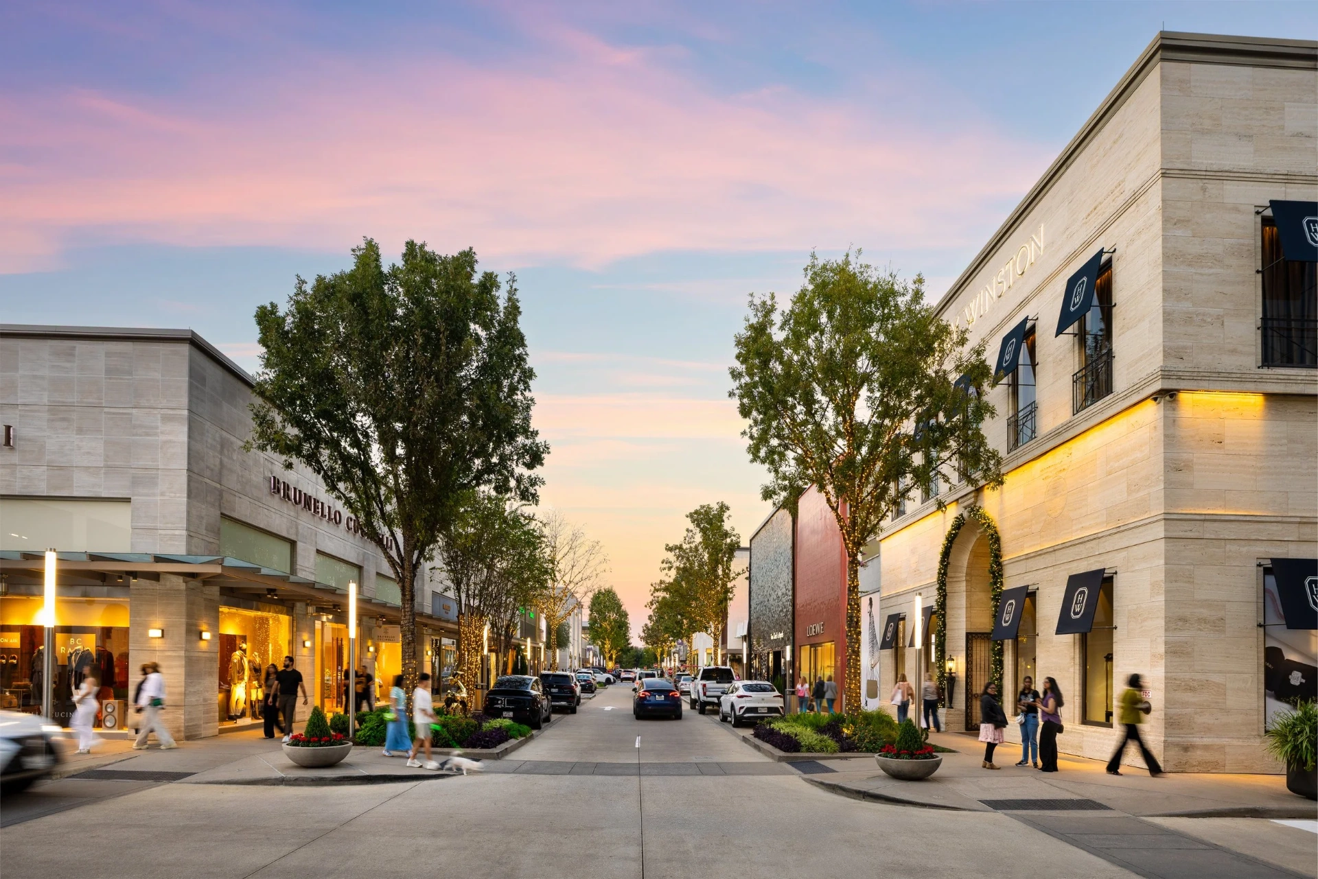 River Oaks District at dusk, an open-air street with Harry Winston, Brunello Cucinelli, and Loewe storefronts under a pink sky