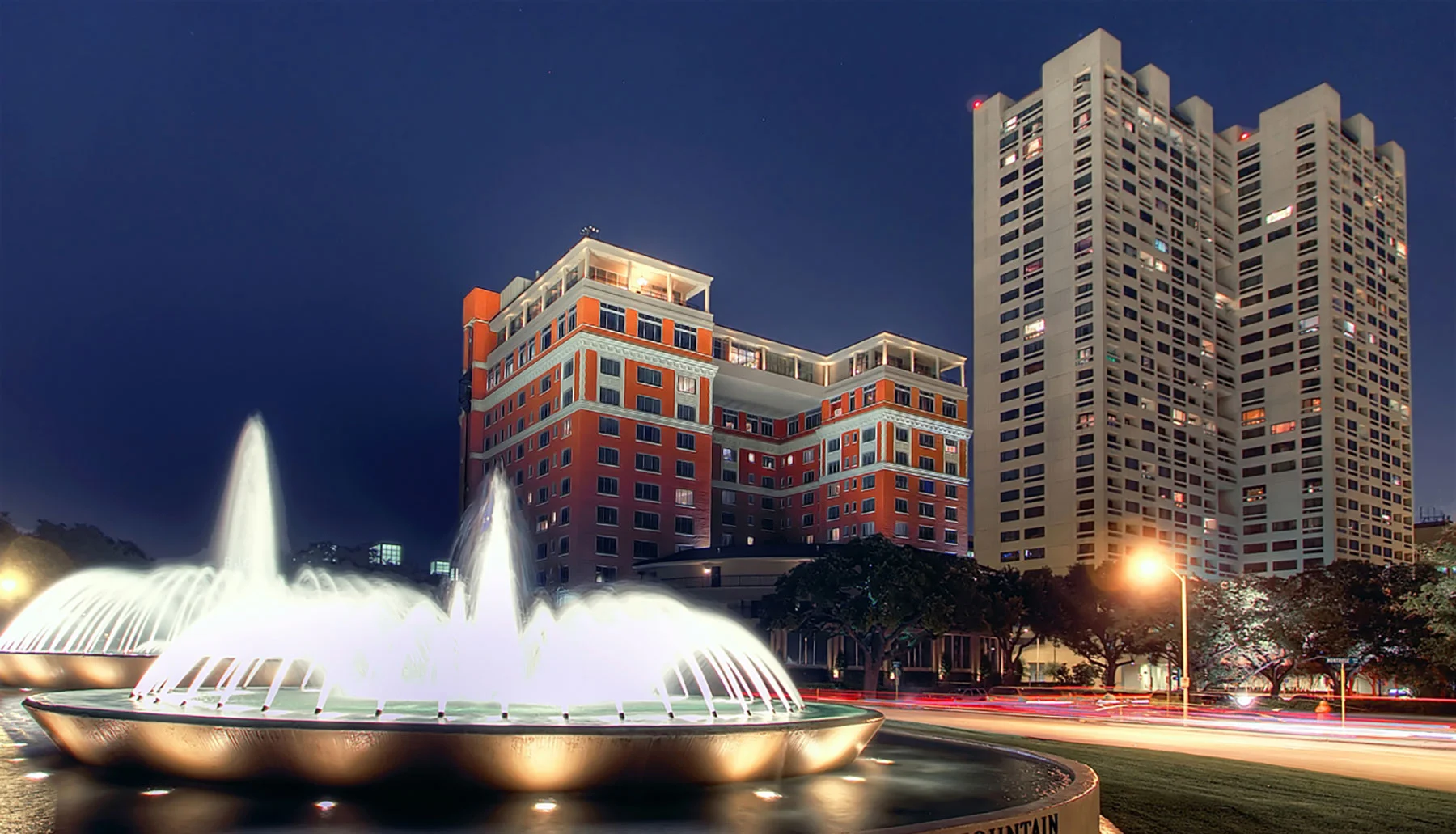 Mecom Fountain illuminated at night with the Warwick Towers behind it in the Museum District
