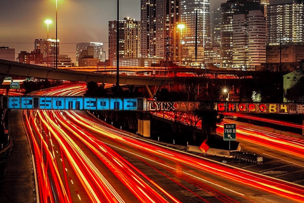 The 'Be Someone' graffiti bridge over Houston's I-45 with downtown skyline at dusk and red light trails